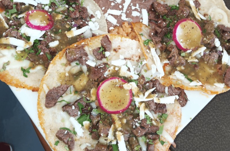 Open tortillas piled with chopped carne asada, radish slices and green salsa.