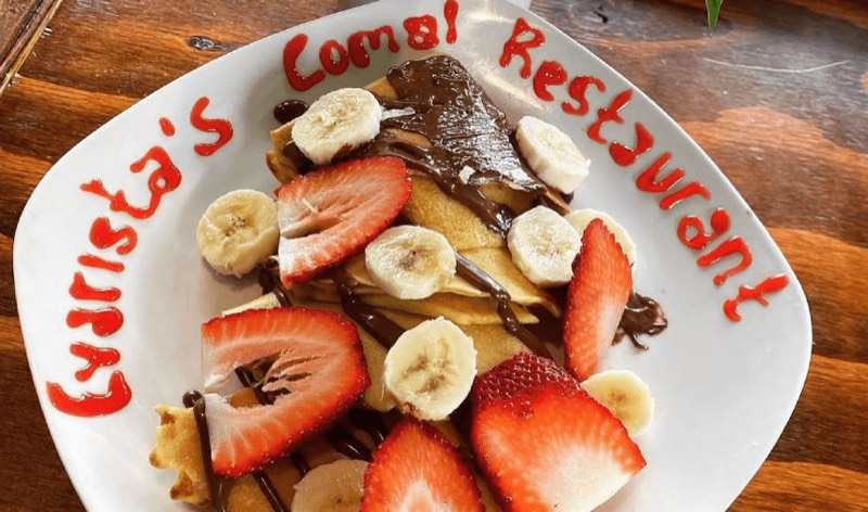 Crepes with strawberries, banana and chocolate, the restaurant's name written in sauce around the plate.