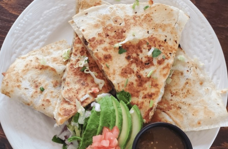 A grilled quesadilla cut in wedges with avocado and salsa.