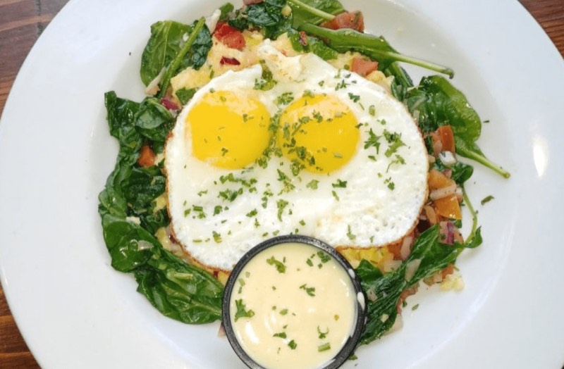 Two fried eggs over sautéed spinach with a cup of hollandaise.