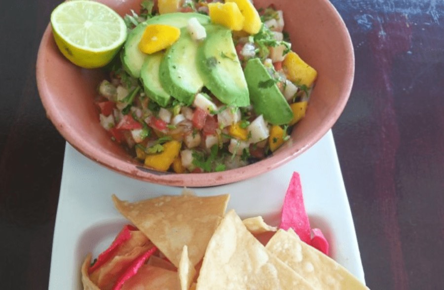 A bowl of guacamole and pico de gallo with tortilla chips.