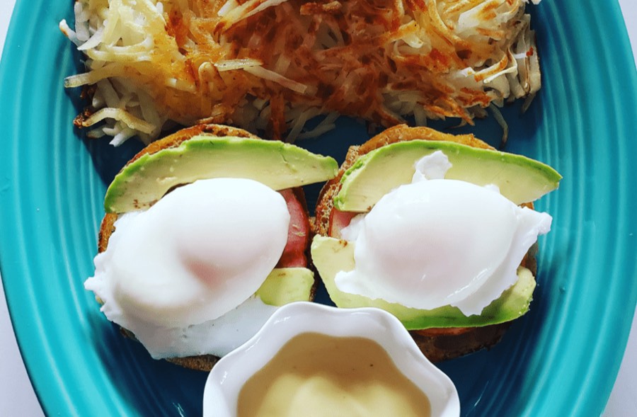 Two poached eggs over avocado with hollandaise on the side and hash browns.