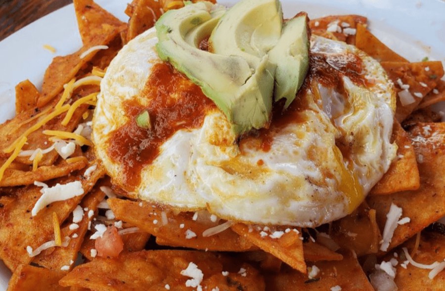 Red chilaquiles topped with a fried egg and sliced avocado.