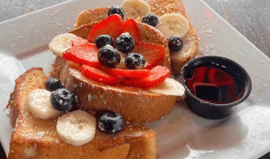 French toast stacked with strawberries, blueberries and banana, with syrup.