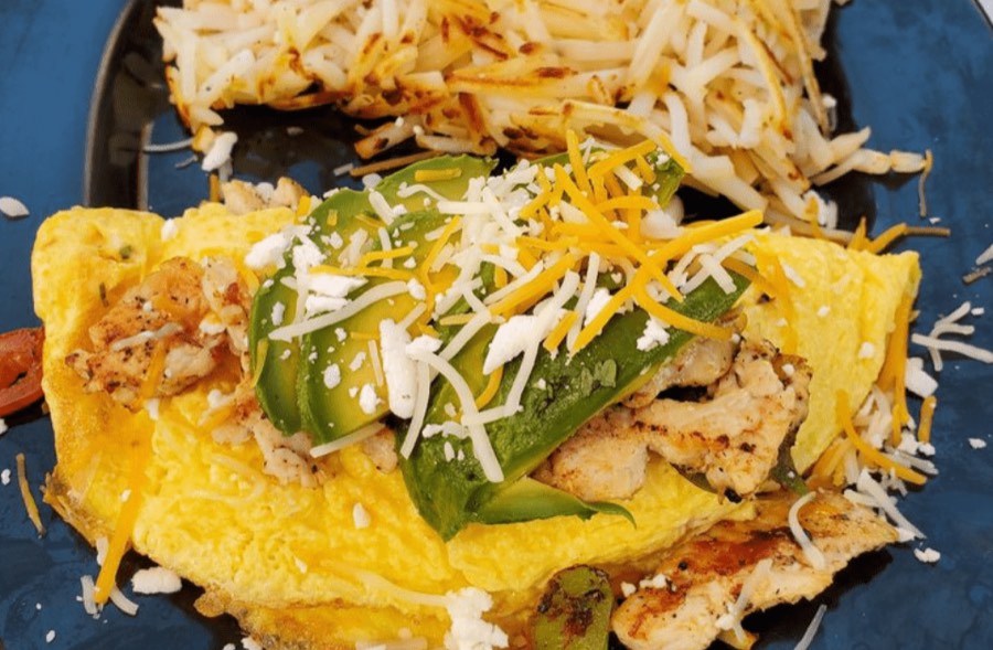 An omelet topped with shredded cheese and avocado, with hash browns.