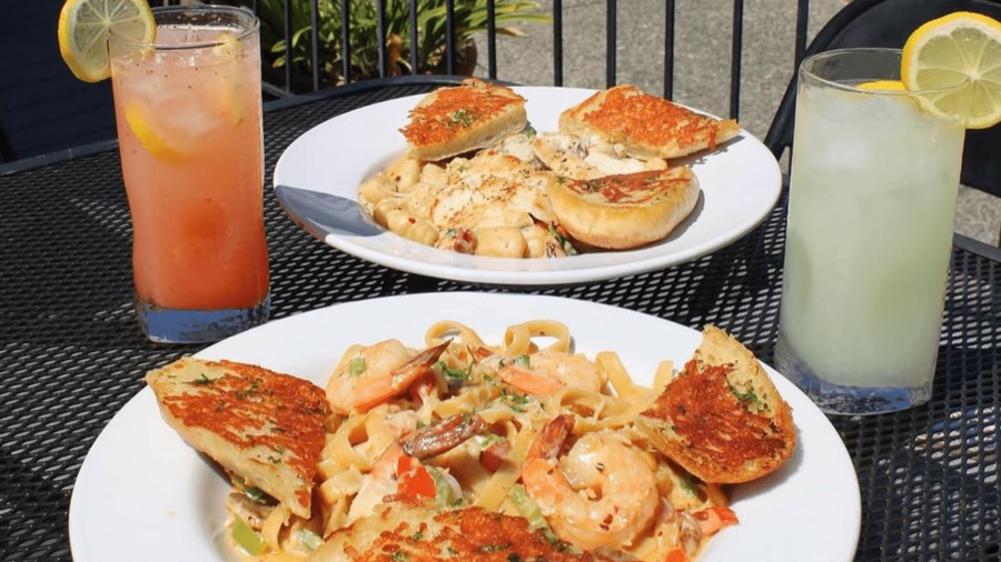 Two plates of prawn pasta with garlic bread and cold drinks on the patio.